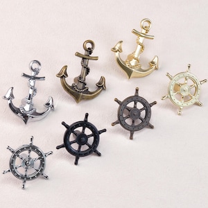 Könnte beinhalten: Eine Auswahl an dekorativer Hardware zum Thema Nautik, darunter Anker und Schiffsräder. Die Anker sind in Silber-, Bronze- und Goldtönen gehalten. Die Schiffsräder sind in Silber-, Bronze- und Schwarz-Ausführungen erhältlich. Diese dekorativen Akzente sind ideal für Küsten- oder Maritimdekor.