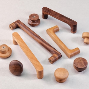 May include: A collection of wooden cabinet hardware, including handles and knobs. The handles are in various styles, with curved and straight designs. The wood tones range from light to dark brown. The knobs are round and mushroom-shaped.
