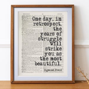 May include: A framed print featuring a quote by Sigmund Freud, "One day, in retrospect, the years of struggle will strike you as the most beautiful." The text is in black, set against a vintage dictionary page.