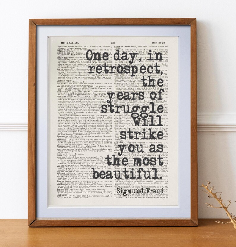 May include: A framed print featuring a quote by Sigmund Freud, "One day, in retrospect, the years of struggle will strike you as the most beautiful." The text is in black, set against a vintage dictionary page.