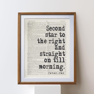 Puede incluir: Impresión enmarcada con la cita "Second star to the right and straight on till morning" de Peter Pan. El texto negro está sobre una página de diccionario vintage, enmarcado en madera marrón.