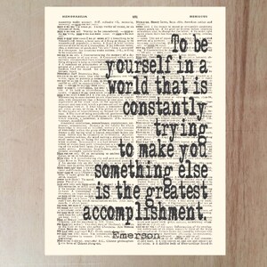 May include: A vintage-style print with a quote by Emerson: "To be yourself in a world that is constantly trying to make you something else is the greatest accomplishment." The text is in black, set against a cream-colored background.