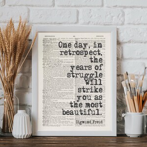 May include: A framed print with the quote "One day, in retrospect, the years of struggle will strike you as the most beautiful" by Sigmund Freud. The text is in black on a vintage newspaper background.