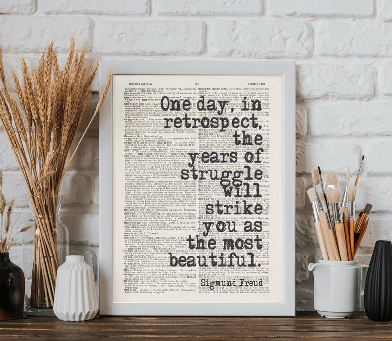 May include: A framed print with the quote "One day, in retrospect, the years of struggle will strike you as the most beautiful" by Sigmund Freud. The text is in black on a vintage newspaper background.