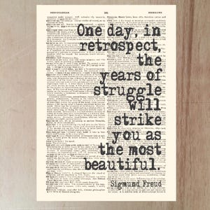 May include: Vintage print featuring a quote by Sigmund Freud: "One day, in retrospect, the years of struggle will strike you as the most beautiful." The text is in black, set against a cream-colored background of dictionary pages.