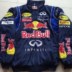Puede incluir: Chaqueta de carreras azul marino con múltiples logotipos de patrocinadores, incluyendo Red Bull, Infiniti y Pepe Jeans. La chaqueta tiene un cuello alto, cierre de cremallera y detalles en rojo y amarillo. Logos de Red Bull en las mangas.