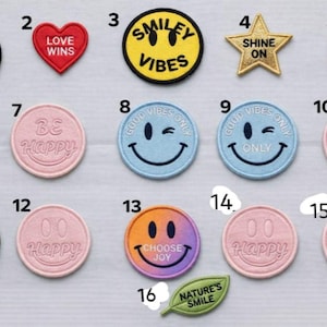 Puede incluir: Colección de parches bordados con mensajes positivos y caras sonrientes. Incluye parches con frases como "Love Wins", "Be Happy" y "Choose Joy". Varios colores y formas, incluyendo corazones, estrellas y círculos.