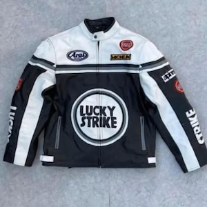 May include: A black and white motorcycle jacket with "LUCKY STRIKE" printed on the front. The jacket has a stand-up collar, multiple patches, and stripes on the sleeves. The jacket is made of leather or a leather-like material.