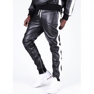 May include: Black leather pants with a white stripe down the side. The pants have a drawstring waist and zippered ankles. The person is wearing white sneakers with red accents. The outfit is a modern take on athletic wear.