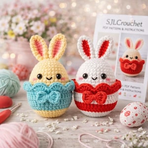 May include: Two crocheted Easter bunny egg ornaments. One is yellow with blue trim, the other is white with red stripes and a red bow. A printed card with instructions is in the background. Decorative Easter theme.