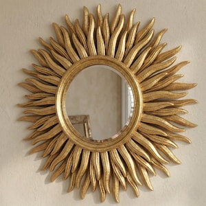 May include: A gold-colored sunburst mirror with a round, reflective center. The mirror's frame features radiating, textured rays, creating a sun-like appearance. The decorative wall mirror is designed to add a touch of elegance to any room.