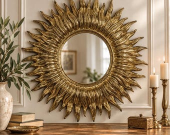 May include: A round wall mirror featuring a decorative gold frame shaped like a sunburst with numerous radiating, textured rays. The central circular glass provides a clear reflection, and the entire piece is finished in a metallic gold tone.