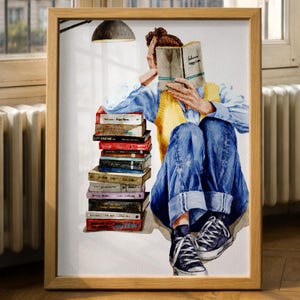 May include: Watercolor painting of a person reading a book, with a stack of books to the left. The person is wearing blue jeans, a yellow vest, and a blue shirt. The book's title is partially visible. The artwork is framed in a wooden frame.