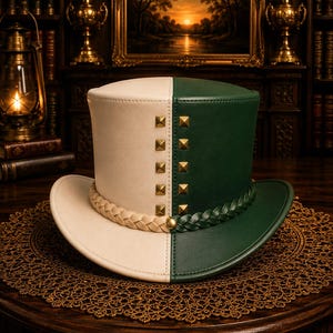 May include: A two-toned top hat featuring a split design with one side in cream and the other in dark green. The hat is adorned with a vertical row of gold-toned square studs and a braided band that transitions from cream to green at the center.