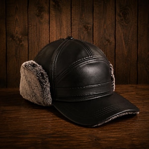 May include: A black leather baseball cap with ear flaps lined with faux fur. The cap has a curved brim and a button on top. The hat is sitting on a wooden surface with a wooden background.