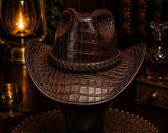 Peut inclure: Un chapeau de cowboy marron foncé présentant un motif texturé en peau de crocodile sur toute la surface. Le chapeau comprend une bande tressée entourant la base de la calotte et un large bord incurvé qui s'incline vers le bas à l'avant et à l'arrière.
