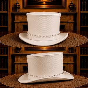 Puede incluir: Dos sombreros de copa blancos con un patr&oacute;n texturizado y una banda de tachuelas plateadas. Los sombreros se exhiben sobre una mesa de madera oscura con una alfombra decorativa marr&oacute;n. El fondo presenta una chimenea, estanter&iacute;as y una pintura.