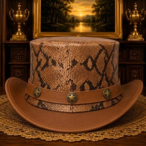 May include: A brown leather cowboy hat with a snakeskin pattern on the crown. The hat has a brown leather band with three star-shaped metal accents. The brim is also brown leather. The hat is displayed on a gold-coloured, lacy doily.