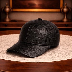 Pode incluir: Boné de beisebol preto com um padrão texturizado semelhante à pele de crocodilo. O boné é feito de um material escuro e está sobre um tapete circular claro em uma mesa de madeira. O fundo inclui um armário de madeira escura e itens decorativos.