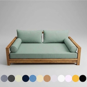 May include: A wooden daybed with a light green cushion and two matching rectangular pillows. Two cylindrical bolster pillows are on each end. The frame is made of light brown wood. A selection of fabric swatches in various colors are at the bottom.