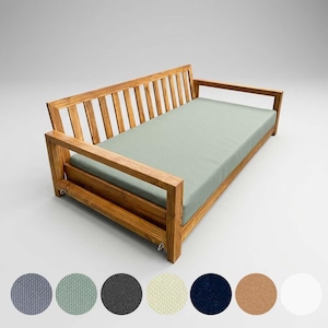 May include: Wooden daybed with a light green mattress. The frame is made of light brown wood. The daybed has a slatted back and armrests. A selection of fabric swatches in various colors are shown below the daybed.