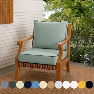May include: Wooden outdoor armchair with light blue cushions and black piping. The chair has a slatted seat and curved armrests. A selection of fabric swatches in various colors are displayed below the chair.