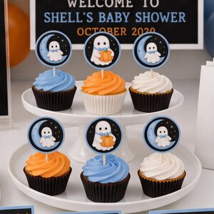 Close-up of Halloween cupcakes decorated with round toppers featuring a little ghost on a blue crescent moon and a ghost holding an orange pumpkin.