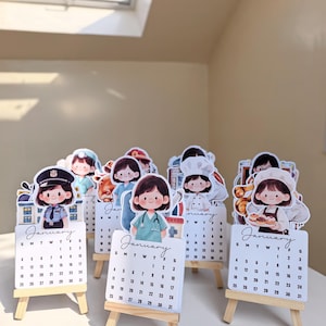 Puede incluir: Una colección de pequeños calendarios blancos con caballetes de madera, cada uno con una profesión diferente. Los calendarios muestran el mes de enero y están decorados con ilustraciones de dibujos animados de personas en varias ocupaciones.