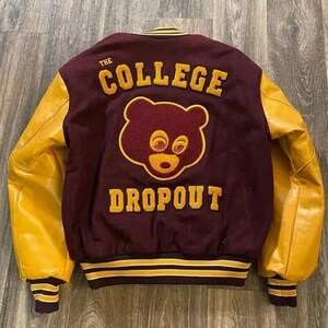 May include: Maroon and gold varsity jacket with the words "THE COLLEGE DROPOUT" and a bear graphic on the back. The sleeves are a bright gold color. The jacket has a striped hem and cuffs.