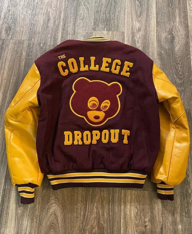 May include: Maroon and gold varsity jacket with the words "THE COLLEGE DROPOUT" and a bear graphic on the back. The sleeves are a bright gold color. The jacket has a striped hem and cuffs.