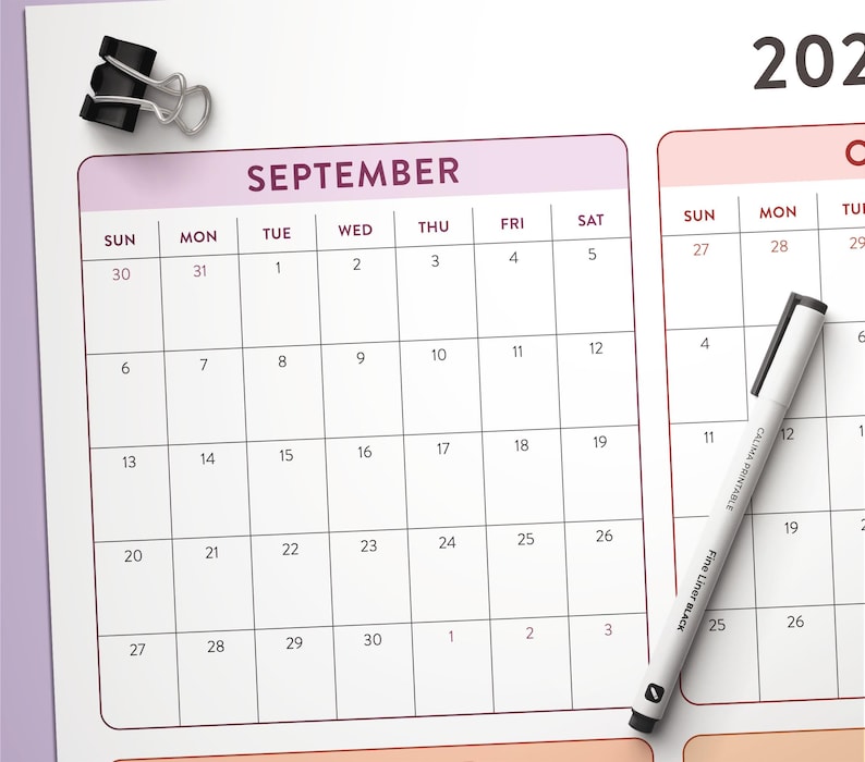 May include: A white paper calendar page for September with a black metal binder clip at the top left corner and a white fine liner pen with black text resting diagonally across the grid. The calendar features a grid layout with black lines.