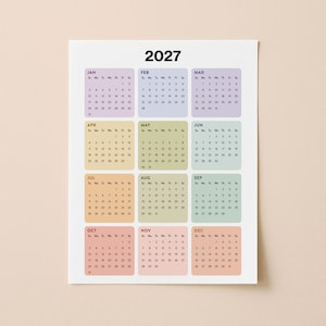 Può includere: Calendario annuale 2027 con layout mensili. Ogni mese è in un colore pastello diverso, con il nome del mese in alto. Il calendario è su sfondo bianco.