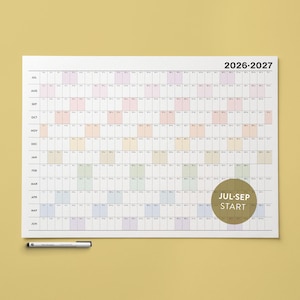 May include: A white wall calendar for 2026-2027 with monthly grids and colour-coded sections. The calendar includes the months from July to June. A circular label reads "JUL-SEP START". A silver pen rests at the bottom.