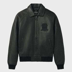 Puede incluir: Chaqueta bomber de cuero negro con cuello, cremallera frontal y pu&ntilde;os y dobladillo de canal&eacute;. Cuenta con un parche en el pecho. La chaqueta tiene el nombre de la marca "AVIREX" en el cuello.