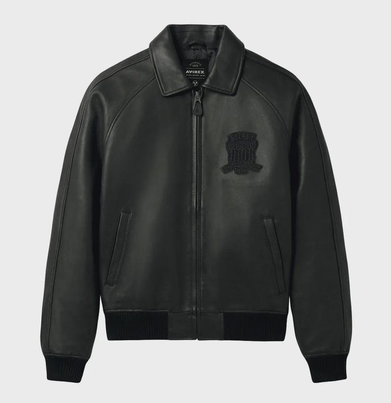 Puede incluir: Chaqueta bomber de cuero negro con cuello, cremallera frontal y pu&ntilde;os y dobladillo de canal&eacute;. Cuenta con un parche en el pecho. La chaqueta tiene el nombre de la marca "AVIREX" en el cuello.