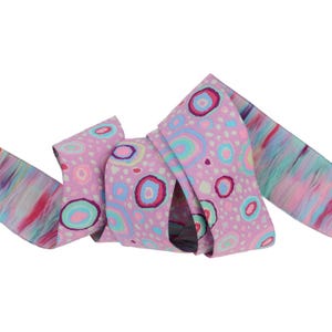 May include: Pink ribbon with a colorful abstract pattern of circles and dots. The ribbon has a light pink background with a white and light blue pattern.