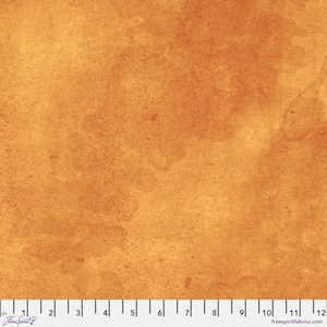 May include: Close-up of a fabric with a watercolor-like effect. The fabric has a warm, golden-brown color with lighter, textured areas. The image includes a ruler along the bottom edge, with the text "freespiritfabrics.com".