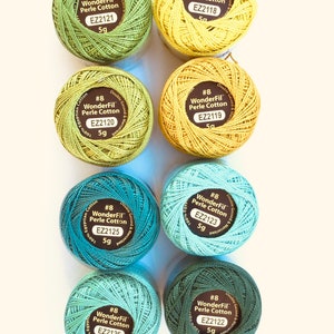 May include: Eight spools of WonderFil Perle Cotton embroidery thread in various shades of green and yellow. Each spool is labeled with the brand name, thread number, and weight. The thread is double gassed and mercerized.
