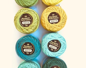 May include: Eight spools of WonderFil Perle Cotton embroidery thread in various shades of green and yellow. Each spool is labeled with the brand name, thread number, and weight. The thread is double gassed and mercerized.