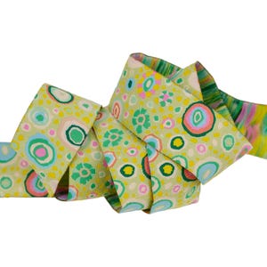 May include: Green ribbon with a colorful abstract pattern of circles and flowers. The ribbon is folded and twisted.