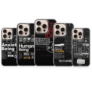 Peut inclure: Plusieurs coques de téléphone noires avec des graphismes et du texte. Les coques présentent des phrases comme "Anxiet Being" et "Human Being", ainsi que des schémas techniques et des avertissements. Design moderne.