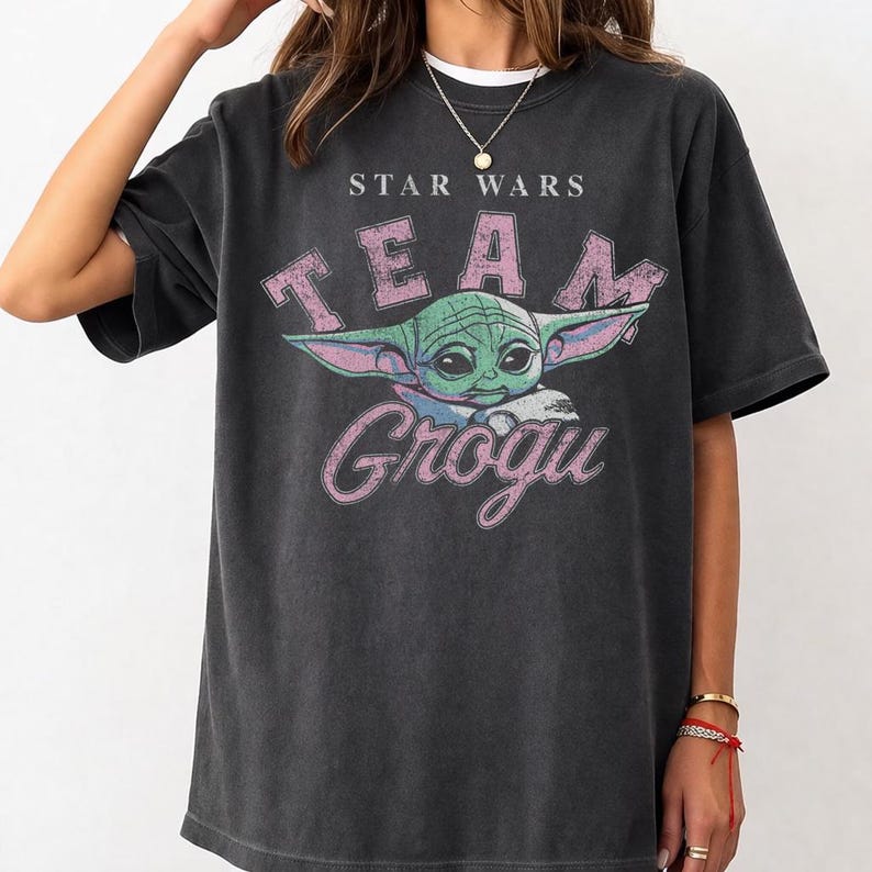 Vintage distressed Grogu graphic design with retro pink typography and cute green alien character illustration on a dark t-shirt in classic bootleg 90s style.