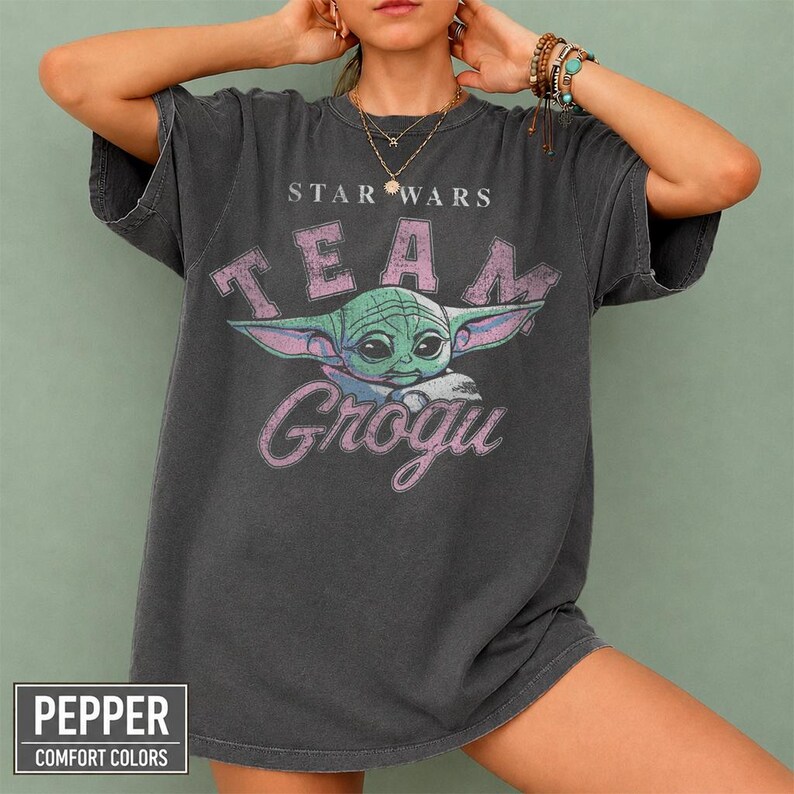 Vintage distressed Grogu graphic design with retro pink typography and cute green alien character illustration on a dark t-shirt in classic bootleg 90s style.