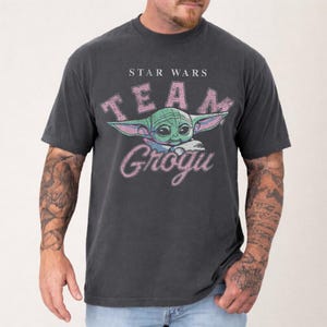 Vintage distressed Grogu graphic design with retro pink typography and cute green alien character illustration on a dark t-shirt in classic bootleg 90s style.