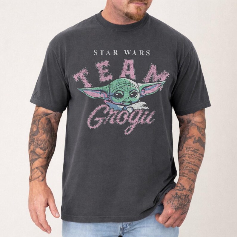 Vintage distressed Grogu graphic design with retro pink typography and cute green alien character illustration on a dark t-shirt in classic bootleg 90s style.