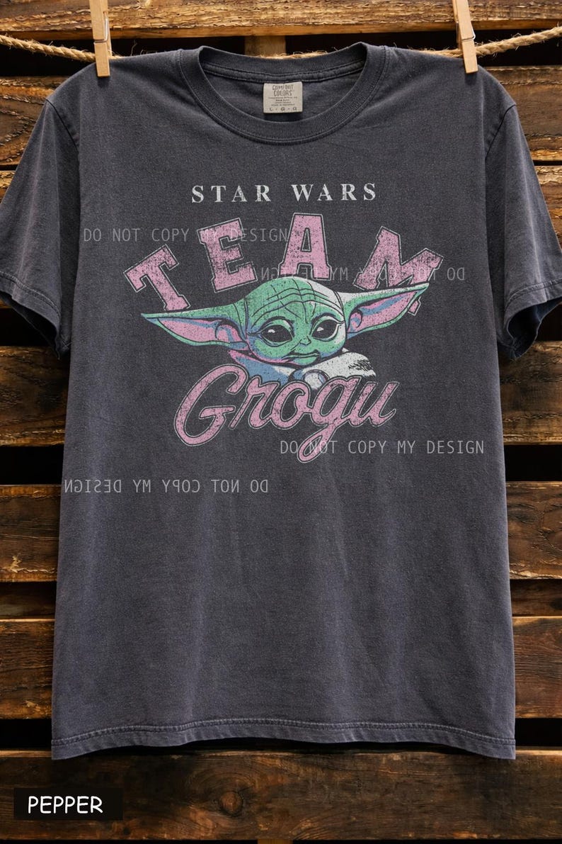 Vintage distressed Grogu graphic design with retro pink typography and cute green alien character illustration on a dark t-shirt in classic bootleg 90s style.