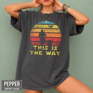 Vintage distressed retro sunset graphic featuring a galactic warrior silhouette with the quote “This Is The Way” on a dark t-shirt design in bootleg vintage style.