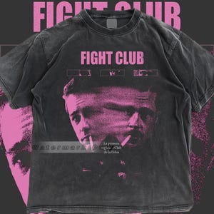 Può includere: T-shirt Fight Club grigio scuro con una grafica rosa di due volti e le parole "FIGHT CLUB" in rosa. La maglietta ha anche testo in spagnolo. Una maglietta in stile vintage.
