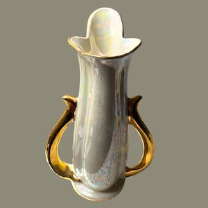 May include: A tall, iridescent ceramic vase featuring a pearlescent finish with subtle rainbow reflections. The vessel has a flared, scalloped rim and two prominent, smooth, solid gold-colored handles extending from the sides to the base.