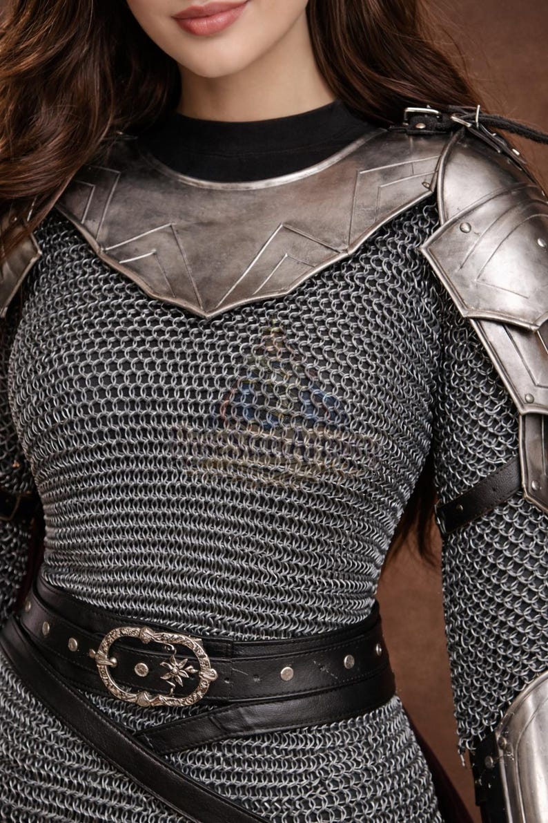 May include: A close-up of a medieval-style costume. The costume features a chainmail shirt, metal shoulder armor, and a black leather belt with a decorative buckle. The armor is silver-toned, and the belt has silver studs.